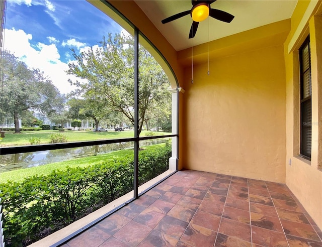 unfurnished sunroom featuring ceiling fan and a water view