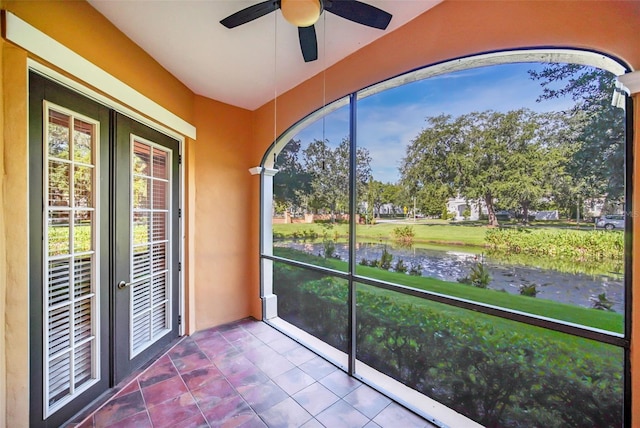 unfurnished sunroom with a water view, ceiling fan, and french doors