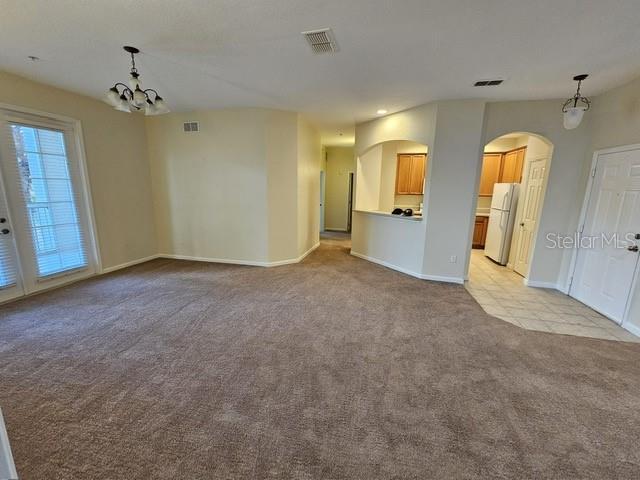 unfurnished living room featuring a chandelier and light colored carpet