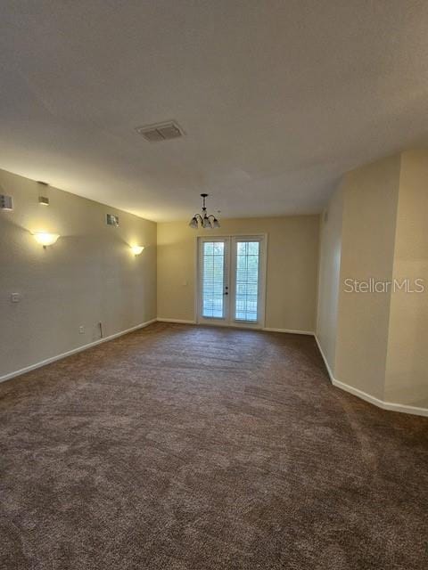 carpeted empty room with a chandelier and french doors