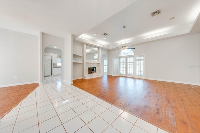 unfurnished living room with ceiling fan, light tile patterned floors, built in features, and a tray ceiling