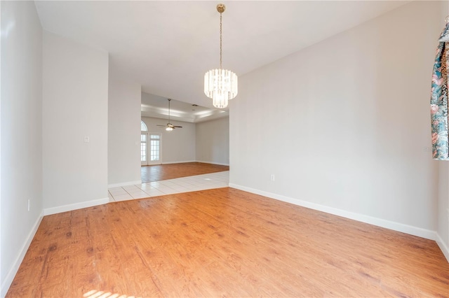 unfurnished room featuring ceiling fan with notable chandelier, a raised ceiling, and light wood-type flooring