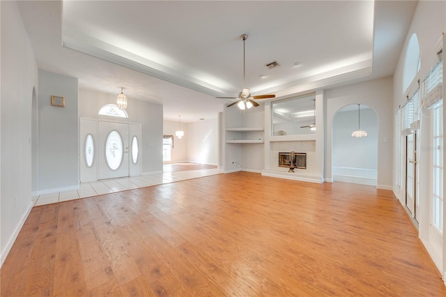 unfurnished living room featuring ceiling fan, light hardwood / wood-style floors, a tray ceiling, built in shelves, and french doors