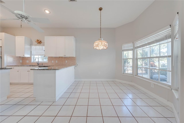 kitchen featuring kitchen peninsula, decorative backsplash, light tile patterned flooring, white cabinets, and light stone counters