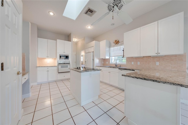 kitchen with a skylight, ceiling fan, white appliances, white cabinets, and a center island