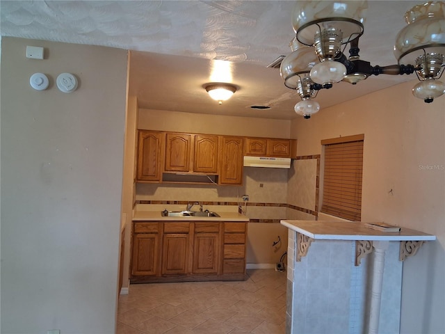 kitchen featuring light countertops, brown cabinetry, under cabinet range hood, and a sink