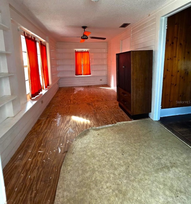 unfurnished room featuring ceiling fan, a textured ceiling, and wood walls