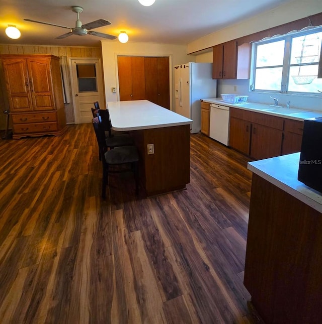 kitchen with ceiling fan, a kitchen island, a kitchen bar, white appliances, and dark wood-type flooring