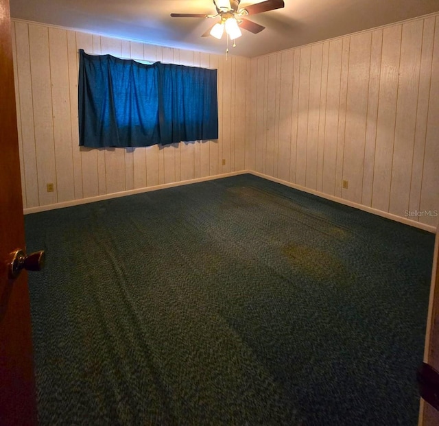 carpeted spare room featuring ceiling fan and wood walls