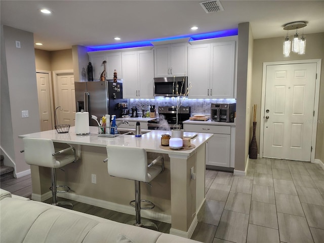 kitchen with white cabinetry, hanging light fixtures, a kitchen island with sink, a breakfast bar area, and stainless steel appliances