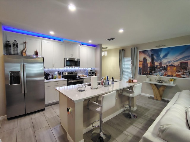 kitchen with white cabinets, a kitchen bar, stainless steel appliances, and a center island with sink