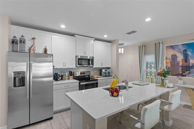 kitchen with sink, light stone counters, a center island with sink, appliances with stainless steel finishes, and white cabinets