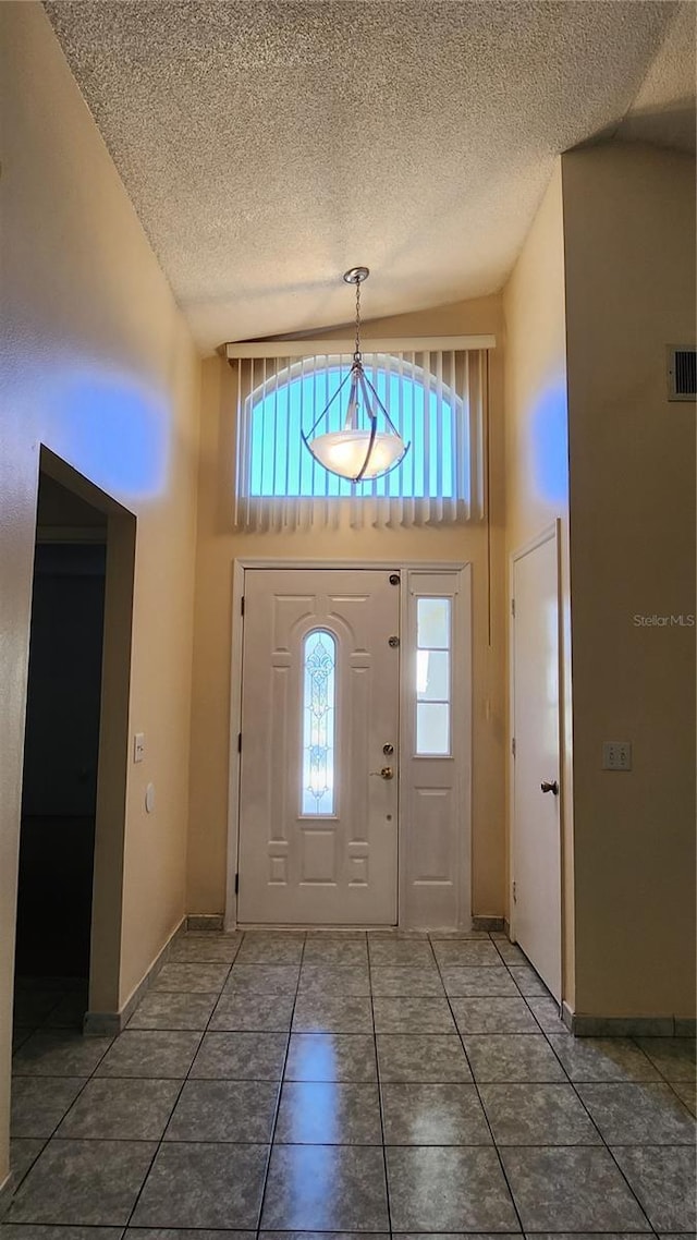 tiled foyer entrance with high vaulted ceiling and a textured ceiling