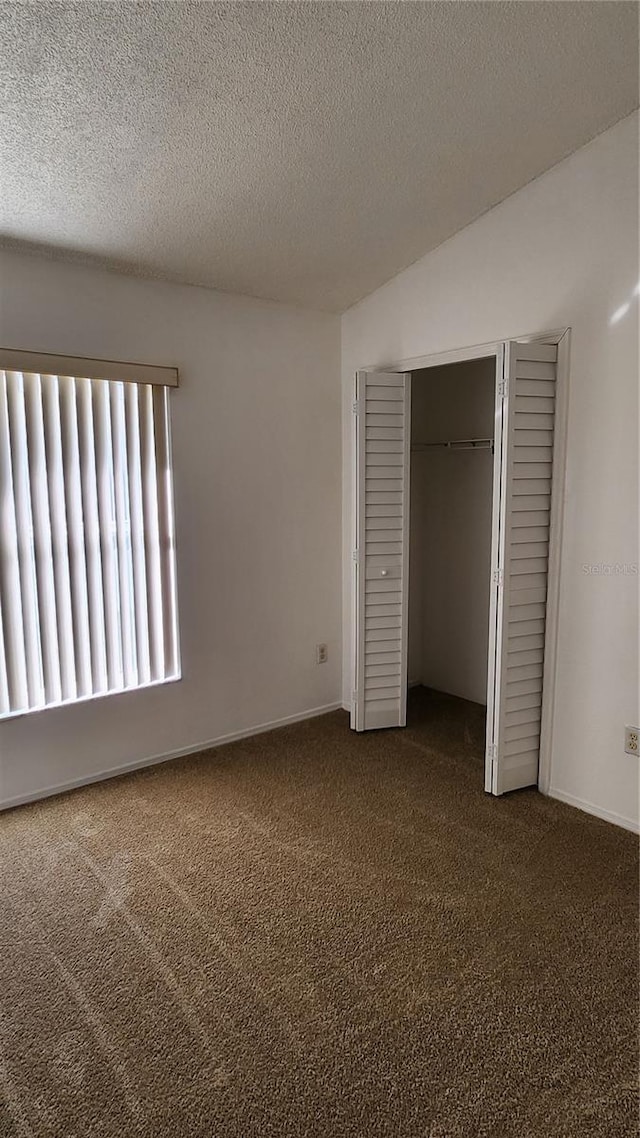 unfurnished bedroom with dark carpet, vaulted ceiling, a closet, and a textured ceiling