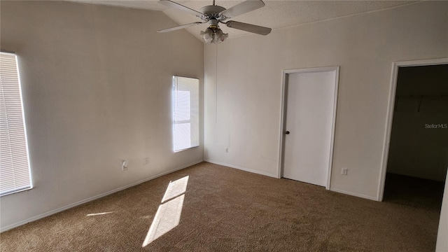 unfurnished bedroom featuring ceiling fan, a spacious closet, vaulted ceiling, and carpet flooring