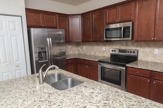 kitchen featuring tasteful backsplash, light stone countertops, sink, and stainless steel appliances