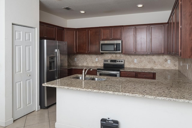 kitchen with light tile patterned floors, kitchen peninsula, stainless steel appliances, light stone countertops, and sink