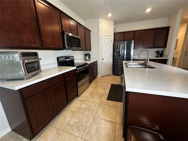 kitchen with light tile patterned flooring, sink, dark brown cabinets, appliances with stainless steel finishes, and an island with sink