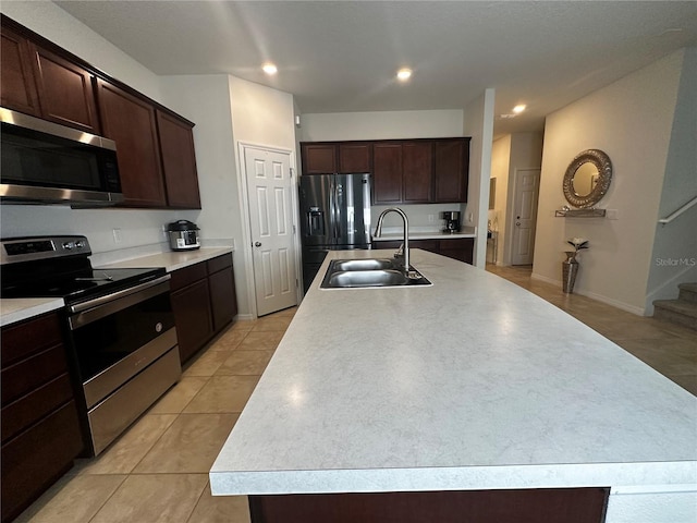 kitchen featuring sink, a kitchen island with sink, dark brown cabinets, stainless steel appliances, and light tile patterned flooring