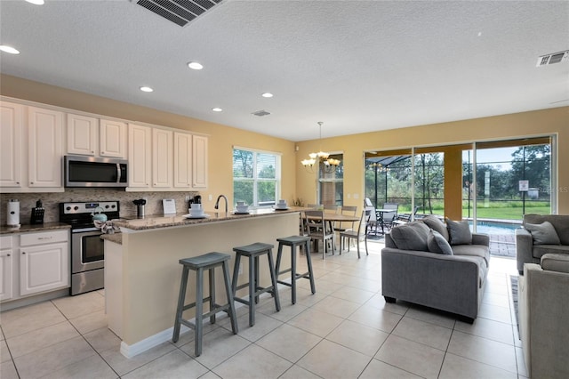 kitchen with pendant lighting, stone countertops, appliances with stainless steel finishes, light tile patterned flooring, and a chandelier