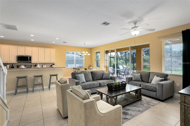 living room featuring ceiling fan with notable chandelier, light tile patterned floors, and a textured ceiling