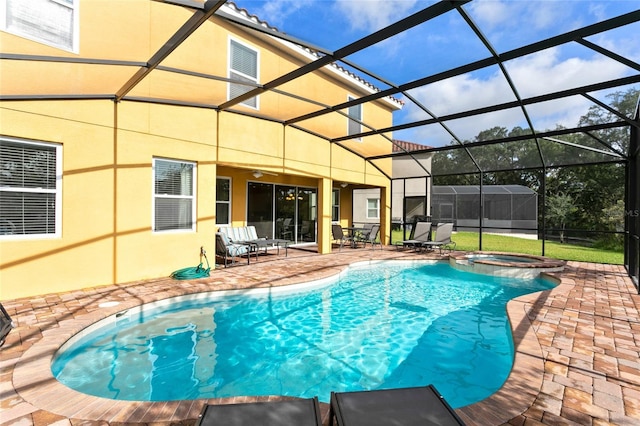 view of pool featuring glass enclosure, an in ground hot tub, and a patio area