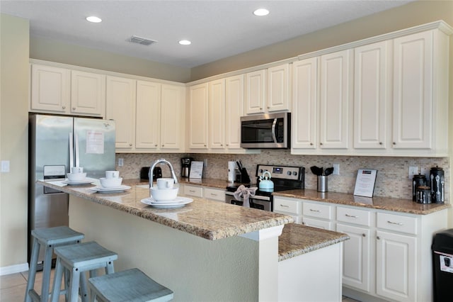 kitchen with stainless steel appliances, white cabinetry, and an island with sink