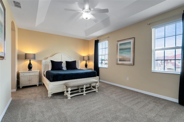 carpeted bedroom with ceiling fan and a raised ceiling