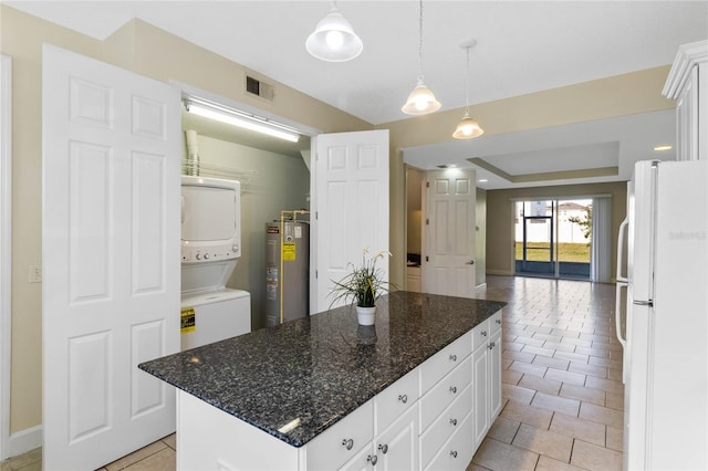 kitchen featuring stacked washer and clothes dryer, a kitchen island, white fridge, and white cabinets