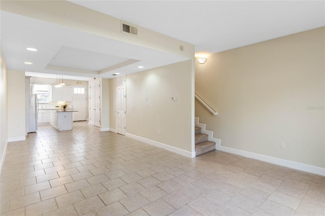 unfurnished living room with light tile patterned floors and a tray ceiling