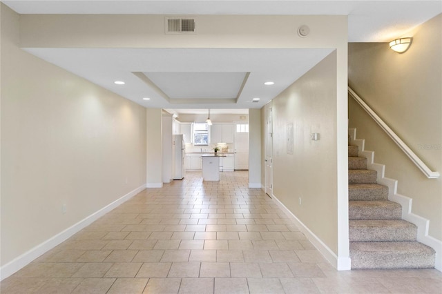 hall featuring a raised ceiling and light tile patterned floors