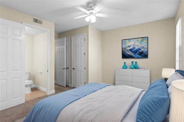 bedroom featuring light carpet, multiple closets, ceiling fan, and ensuite bathroom