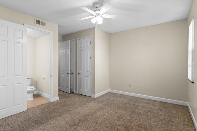 unfurnished bedroom featuring ensuite bathroom, two closets, light carpet, and ceiling fan