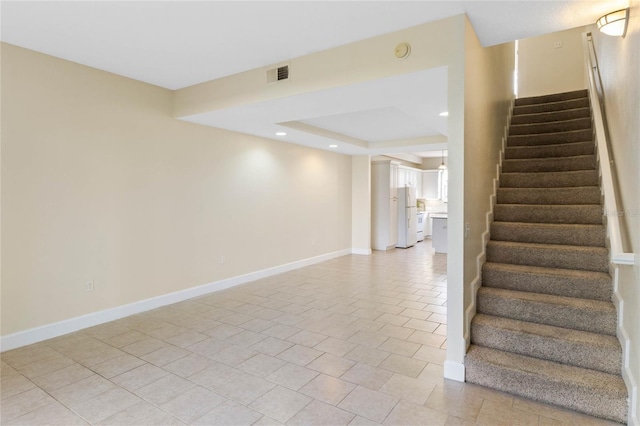 stairway with a raised ceiling and tile patterned flooring