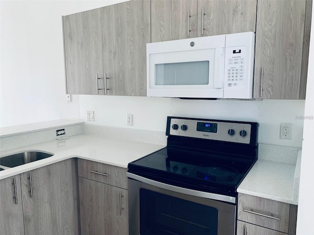 kitchen featuring stainless steel electric range oven, light stone counters, sink, and light brown cabinets