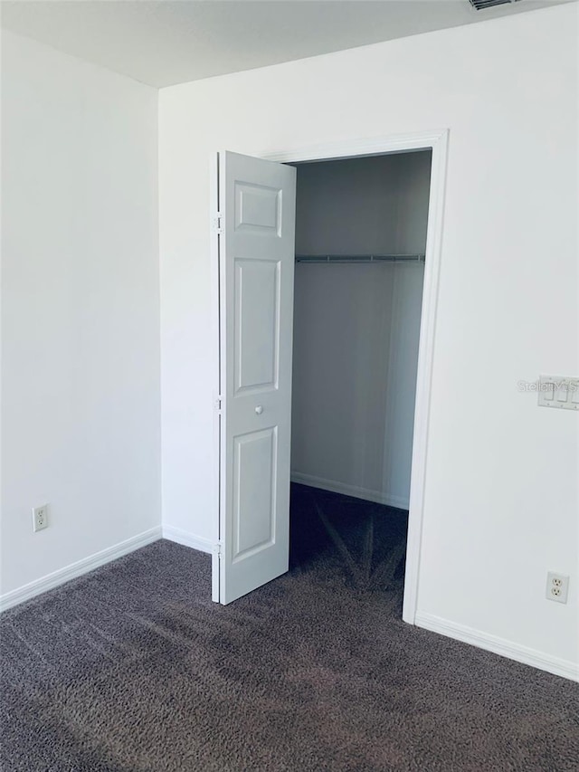 unfurnished bedroom with dark carpet and a closet