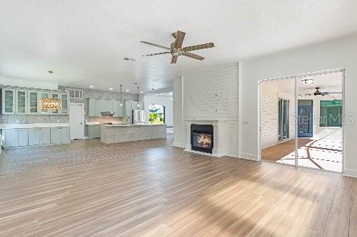 unfurnished living room featuring light wood-type flooring, ceiling fan, a large fireplace, and a textured ceiling