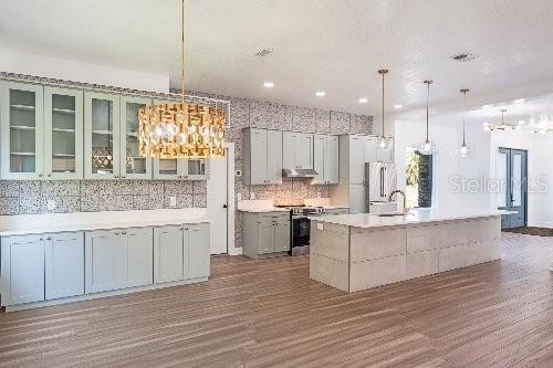 kitchen with appliances with stainless steel finishes, an island with sink, and decorative light fixtures