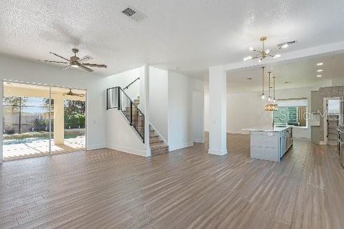 unfurnished living room featuring wood-type flooring, ceiling fan with notable chandelier, and a textured ceiling