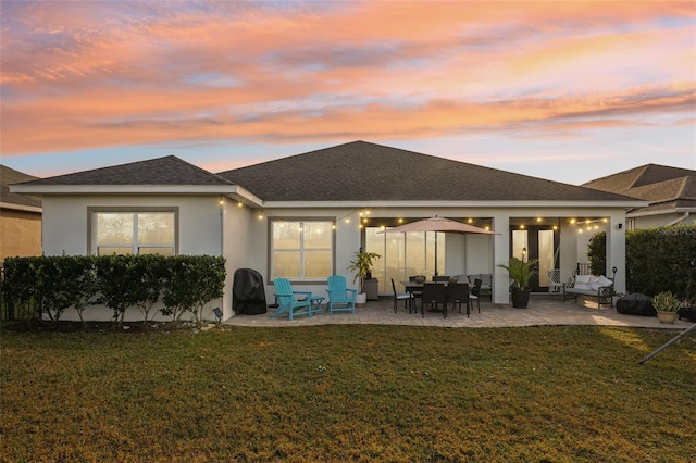 back house at dusk featuring a patio and a lawn