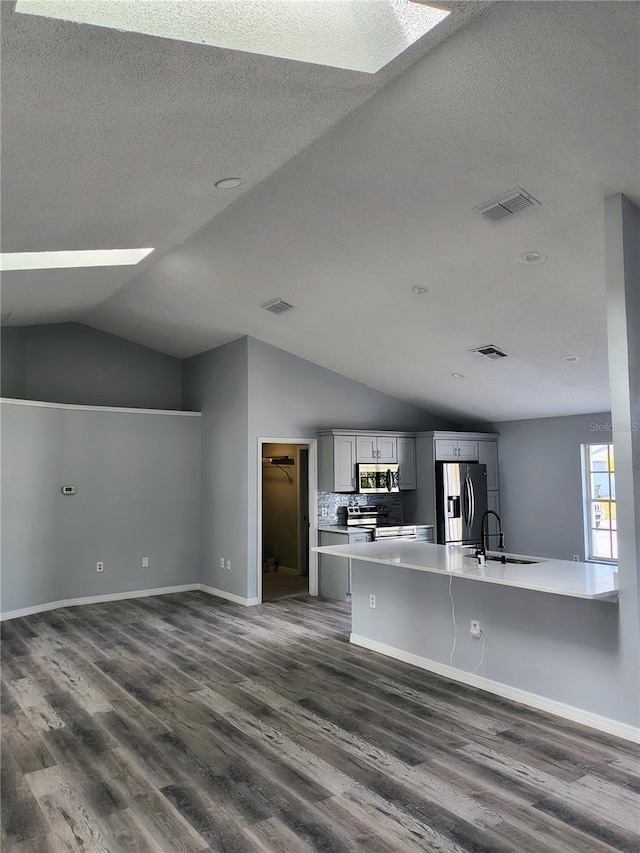 kitchen with backsplash, vaulted ceiling with skylight, dark hardwood / wood-style floors, appliances with stainless steel finishes, and gray cabinetry