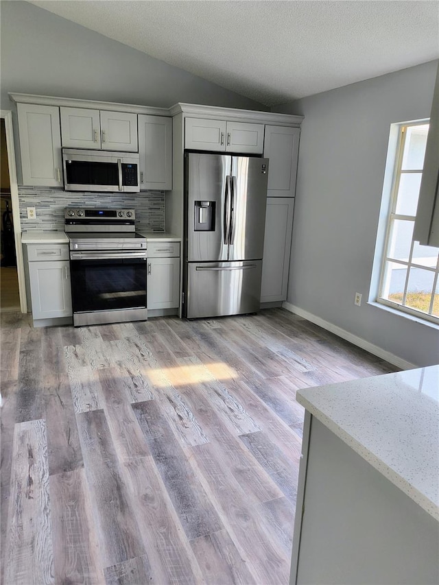 kitchen featuring a textured ceiling, stainless steel appliances, tasteful backsplash, vaulted ceiling, and light stone counters