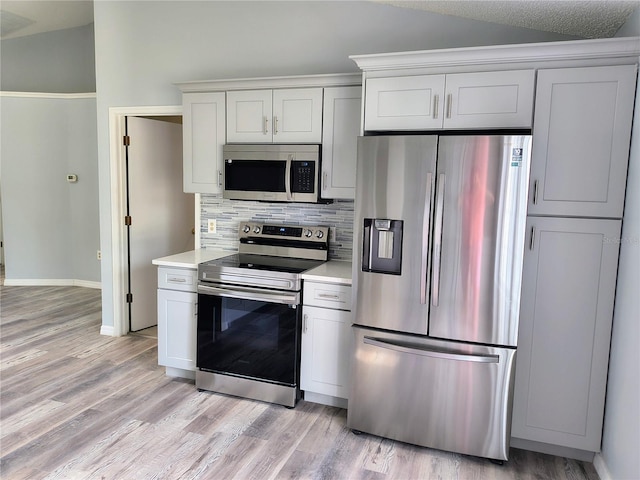 kitchen featuring backsplash, vaulted ceiling, appliances with stainless steel finishes, and white cabinetry