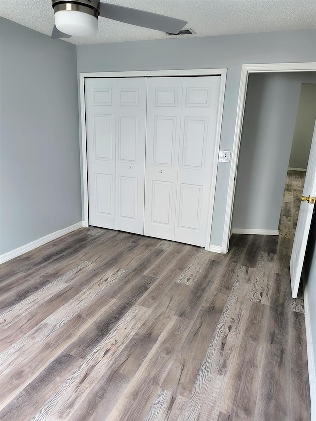 unfurnished bedroom featuring ceiling fan, a closet, dark wood-type flooring, and a textured ceiling