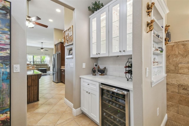 bar featuring stainless steel refrigerator, wine cooler, white cabinets, light tile patterned flooring, and decorative backsplash