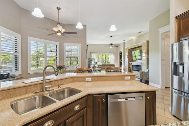 kitchen featuring a tile fireplace, sink, light tile patterned floors, ceiling fan, and stainless steel appliances