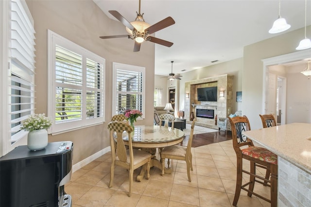 dining space featuring light tile patterned flooring, ceiling fan, and a stone fireplace