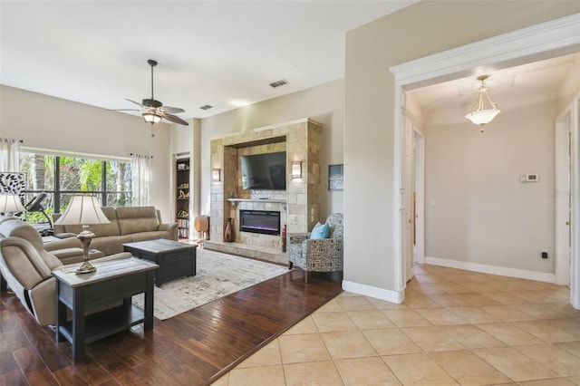 tiled living room with a tile fireplace and ceiling fan