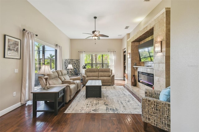 living room with dark wood-type flooring, ceiling fan, and a tile fireplace