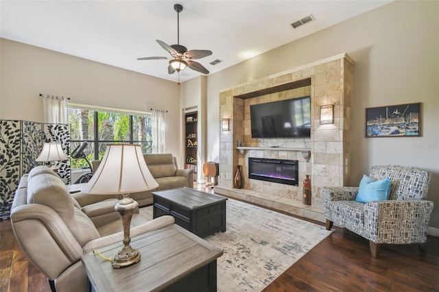 living room featuring a stone fireplace, dark wood-type flooring, and ceiling fan